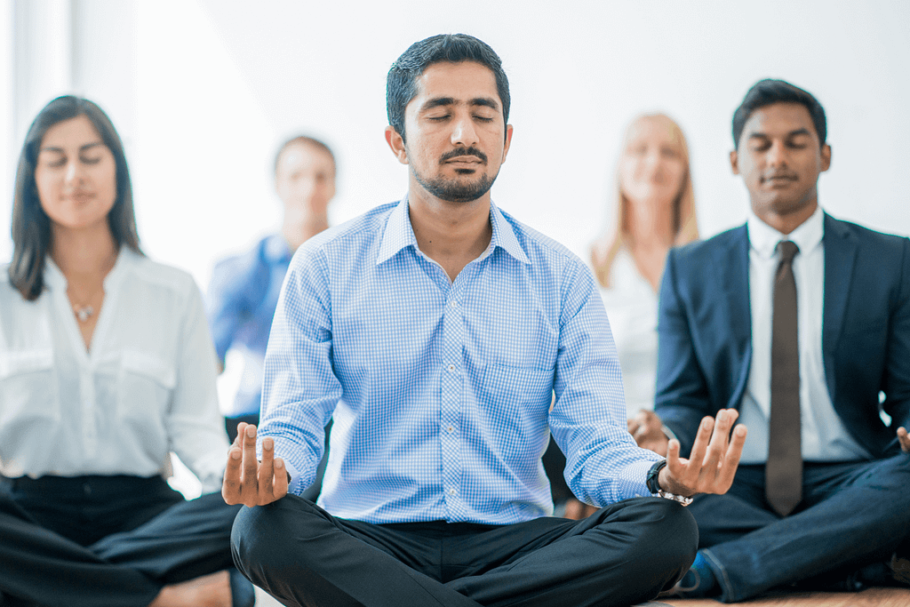 a group of professionally dressed employees meditating at work