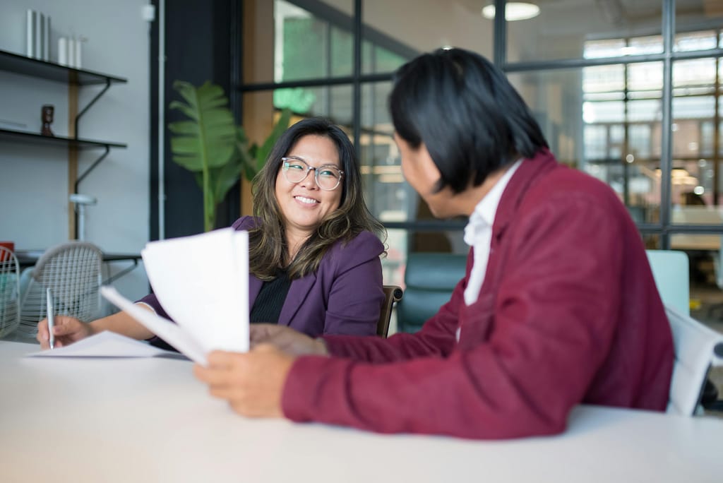Two employees conversing at a desk taking notes regarding the wellness programs and boosting moral.
