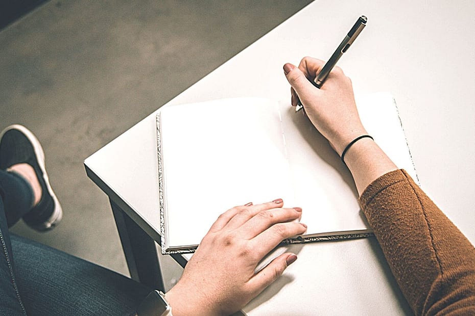 Close up of a woman in a brown sweater holding a pen beginning to write in a journal. Questions to ask while evaluating a wellness program