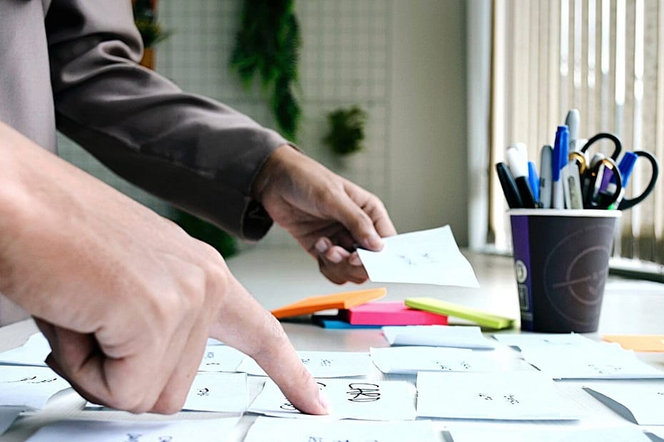 Sideview of a person placing sticky notes on a table with a cup of pens.