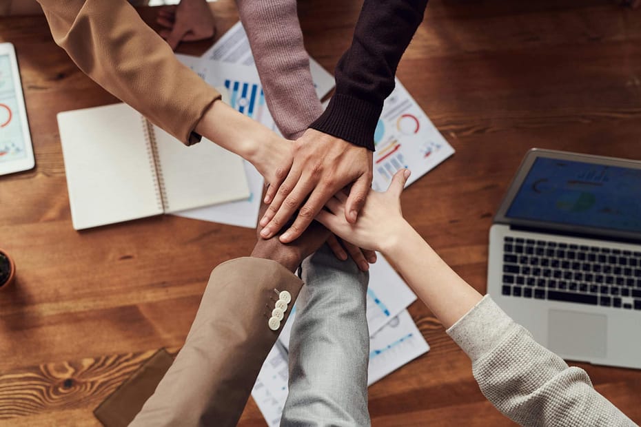 Employees putting hands together in celebration after a successful DEI meeting. Team-building activities that promote diversity, equity, and inclusion help employees build trust, strengthen collaboration, encourage belonging, and create a more inclusive workplace culture.
