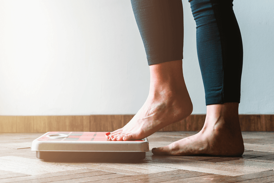 Person stepping onto a scale to track progress, illustrating how measuring outcomes and engagement is essential for identifying gaps in a workplace wellness program.